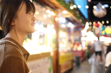 Doğu Asyalı kadın gece pazarından alışveriş yapıyor. Sokaktan gelen ışıkları arka planı aydınlatıyor..