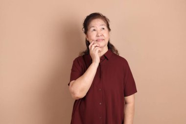 Kahverengi arka planda duran koyu kırmızı tişörtlü kıdemli Doğu Asyalı kadın..