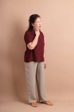 Senior East Asian woman with a deep red shirt standing against a brown background. clipart