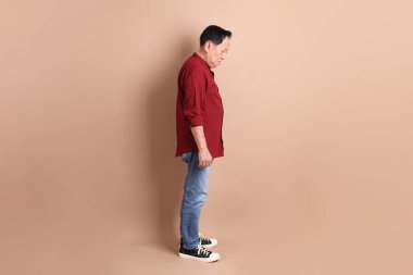 Kahverengi arka planda duran koyu kırmızı gömlekli kıdemli Doğu Asyalı adam..