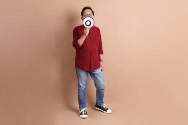 Kahverengi arka planda duran koyu kırmızı gömlekli kıdemli Doğu Asyalı adam..