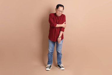 Kahverengi arka planda duran koyu kırmızı gömlekli kıdemli Doğu Asyalı adam..