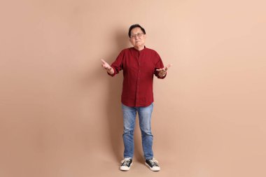 Kahverengi arka planda duran koyu kırmızı gömlekli kıdemli Doğu Asyalı adam..