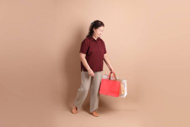 Kahverengi arka planda duran koyu kırmızı tişörtlü kıdemli Doğu Asyalı kadın..