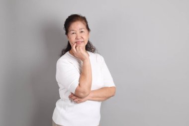 Beyaz gömlekli üst düzey Doğu Asyalı kadın gri arka planda duruyor..