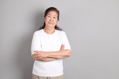 Beyaz gömlekli üst düzey Doğu Asyalı kadın gri arka planda duruyor..