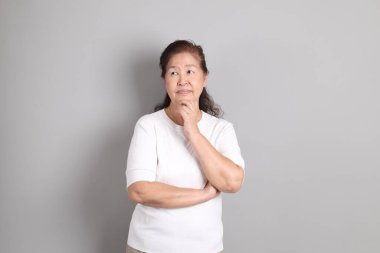 Beyaz gömlekli üst düzey Doğu Asyalı kadın gri arka planda duruyor..