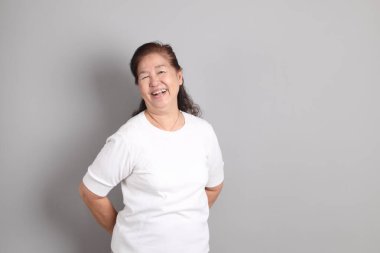 Beyaz gömlekli üst düzey Doğu Asyalı kadın gri arka planda duruyor..