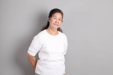 Beyaz gömlekli üst düzey Doğu Asyalı kadın gri arka planda duruyor..