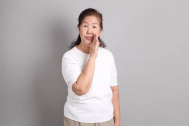 Beyaz gömlekli üst düzey Doğu Asyalı kadın gri arka planda duruyor..