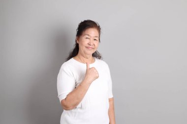 Beyaz gömlekli üst düzey Doğu Asyalı kadın gri arka planda duruyor..