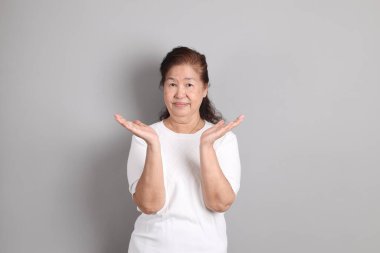 Beyaz gömlekli üst düzey Doğu Asyalı kadın gri arka planda duruyor..