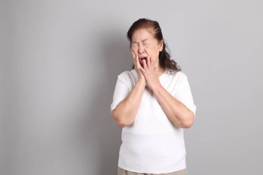 Beyaz gömlekli üst düzey Doğu Asyalı kadın gri arka planda duruyor..