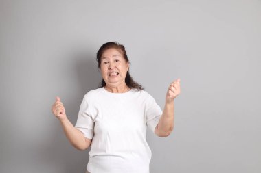 Beyaz gömlekli üst düzey Doğu Asyalı kadın gri arka planda duruyor..