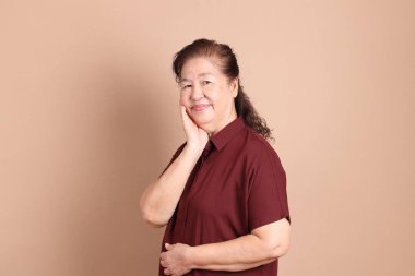 Kahverengi arka planda duran koyu kırmızı gömlekli kıdemli Doğu Asyalı adam..