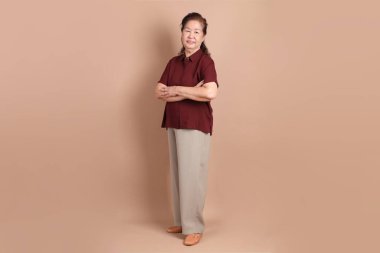 Kahverengi arka planda duran koyu kırmızı gömlekli kıdemli Doğu Asyalı adam..