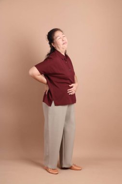 Kahverengi arka planda duran koyu kırmızı gömlekli kıdemli Doğu Asyalı adam..