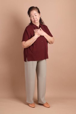 Kahverengi arka planda duran koyu kırmızı gömlekli kıdemli Doğu Asyalı adam..