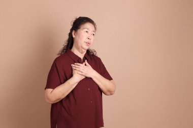 Kahverengi arka planda duran koyu kırmızı gömlekli kıdemli Doğu Asyalı adam..