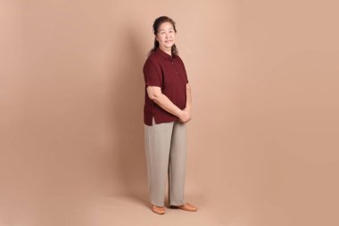 Kahverengi arka planda duran koyu kırmızı gömlekli kıdemli Doğu Asyalı adam..