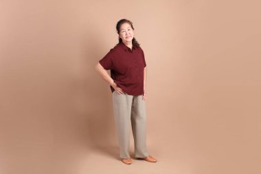 Kahverengi arka planda duran koyu kırmızı gömlekli kıdemli Doğu Asyalı adam..