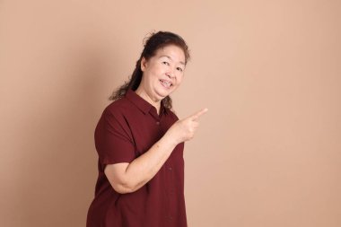 Kahverengi arka planda duran koyu kırmızı gömlekli kıdemli Doğu Asyalı adam..