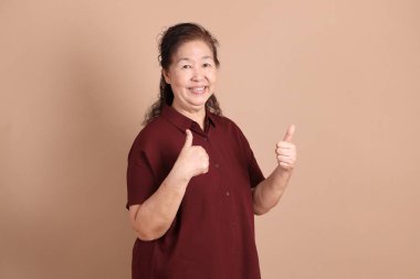 Kahverengi arka planda duran koyu kırmızı gömlekli kıdemli Doğu Asyalı adam..