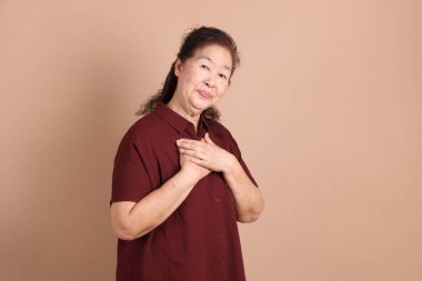 Kahverengi arka planda duran koyu kırmızı gömlekli kıdemli Doğu Asyalı adam..