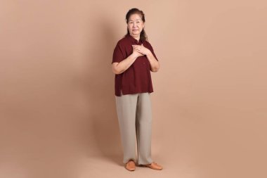 Kahverengi arka planda duran koyu kırmızı gömlekli kıdemli Doğu Asyalı adam..