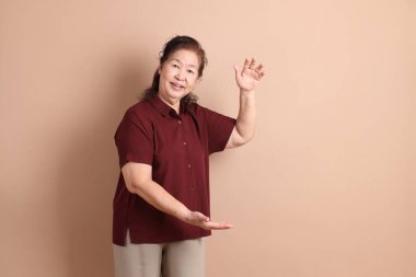 Kahverengi arka planda duran koyu kırmızı gömlekli kıdemli Doğu Asyalı adam..