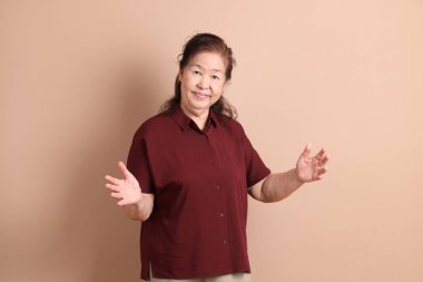 Kahverengi arka planda duran koyu kırmızı gömlekli kıdemli Doğu Asyalı adam..