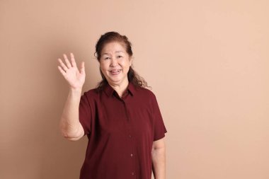 Kahverengi arka planda duran koyu kırmızı gömlekli kıdemli Doğu Asyalı adam..