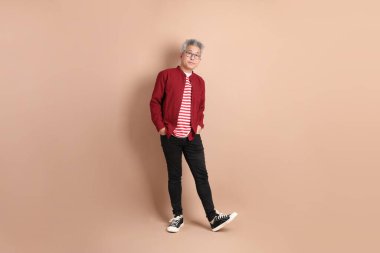 Kahverengi arka planda duran koyu kırmızı gömlekli kıdemli Doğu Asyalı adam..