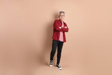 Kahverengi arka planda duran koyu kırmızı gömlekli kıdemli Doğu Asyalı adam..