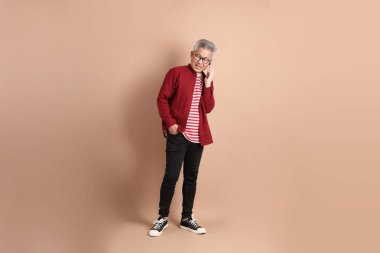 Kahverengi arka planda duran koyu kırmızı gömlekli kıdemli Doğu Asyalı adam..