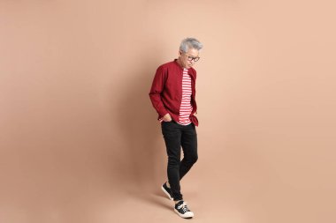 Kahverengi arka planda duran koyu kırmızı gömlekli kıdemli Doğu Asyalı adam..