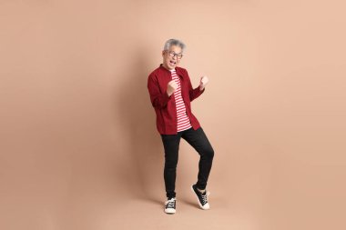 Kahverengi arka planda duran koyu kırmızı gömlekli kıdemli Doğu Asyalı adam..