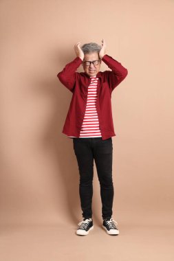 Kahverengi arka planda duran koyu kırmızı gömlekli kıdemli Doğu Asyalı adam..