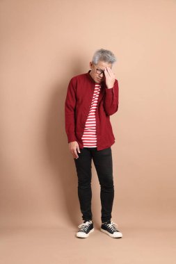 Kahverengi arka planda duran koyu kırmızı gömlekli kıdemli Doğu Asyalı adam..