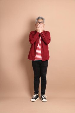 Kahverengi arka planda duran koyu kırmızı gömlekli kıdemli Doğu Asyalı adam..