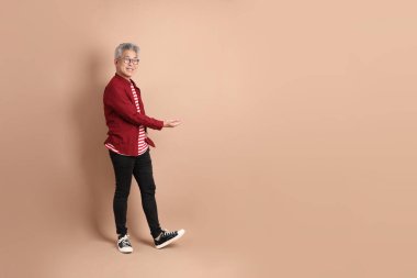 Kahverengi arka planda duran koyu kırmızı gömlekli kıdemli Doğu Asyalı adam..