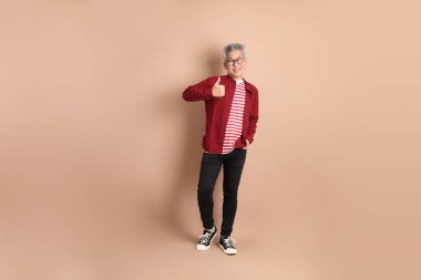 Kahverengi arka planda duran koyu kırmızı gömlekli kıdemli Doğu Asyalı adam..