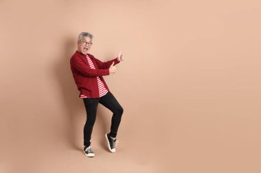 Kahverengi arka planda duran koyu kırmızı gömlekli kıdemli Doğu Asyalı adam..