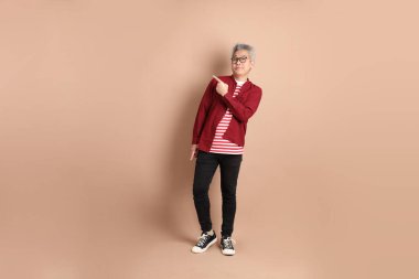 Kahverengi arka planda duran koyu kırmızı gömlekli kıdemli Doğu Asyalı adam..