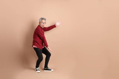 Kahverengi arka planda duran koyu kırmızı gömlekli kıdemli Doğu Asyalı adam..