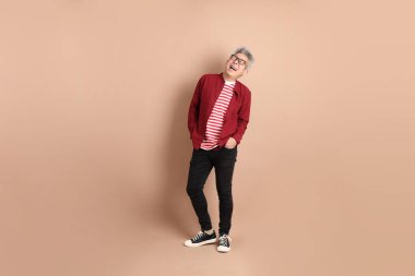 Kahverengi arka planda duran koyu kırmızı gömlekli kıdemli Doğu Asyalı adam..