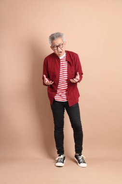 Kahverengi arka planda duran koyu kırmızı gömlekli kıdemli Doğu Asyalı adam..