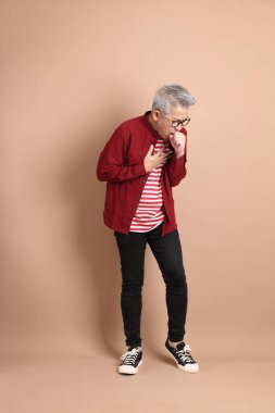 Kahverengi arka planda duran koyu kırmızı gömlekli kıdemli Doğu Asyalı adam..