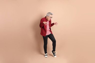 Kahverengi arka planda duran koyu kırmızı gömlekli kıdemli Doğu Asyalı adam..