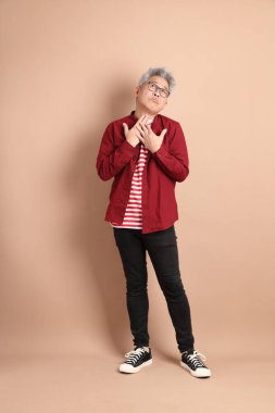 Kahverengi arka planda duran koyu kırmızı gömlekli kıdemli Doğu Asyalı adam..